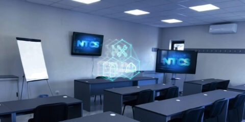 Un'aula moderna a Napoli con un icone di una fabbrica, strumenti e un capo di abbigliamento che fluttuano a mezz'aria. Due grandi schermi visualizzano "NTCS". L'aula, progettata per i corsi NTCS per la sicurezza sul lavoro, comprende diverse file di scrivanie e sedie, una lavagna e un condizionatore montato a parete.